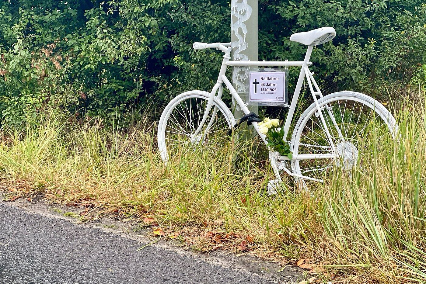 ein weißes Geisterrad mit Schild und weißen Rosen am Straßenrand