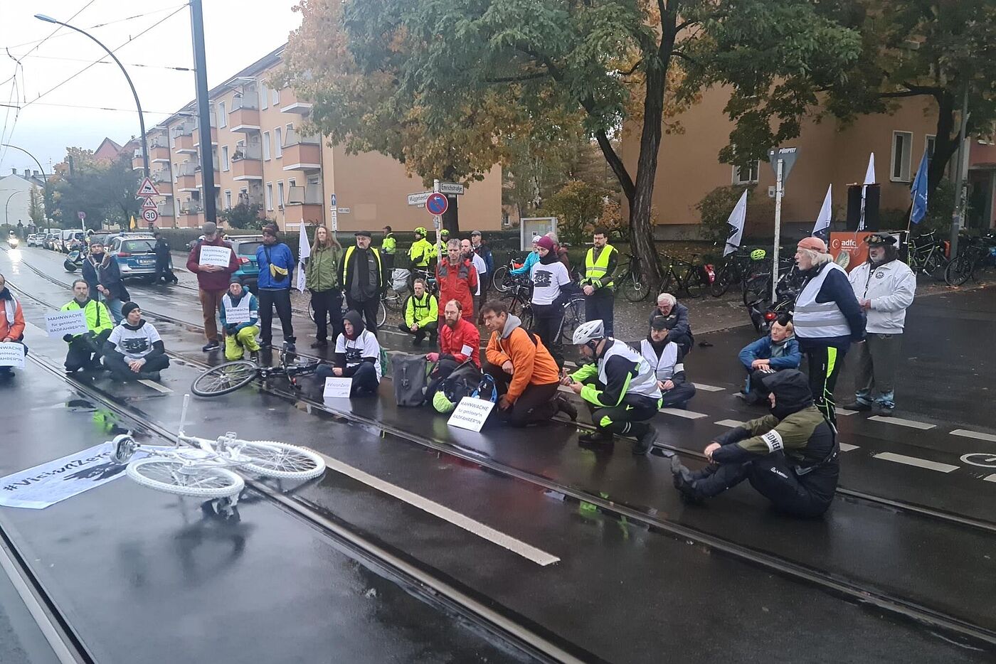 Menschen sitzen bei einer Mahnwache auf der Straße um ein weißes Geisterrad