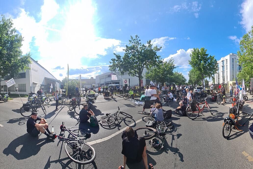 Menschen sitzen bei einer Mahnwache auf dem Boden um ein weißes Fahrrad