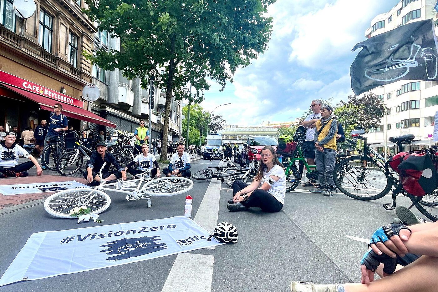 Menschen sitzen um ein weißes Geisterrad und eine Fahne mit Vision Zero