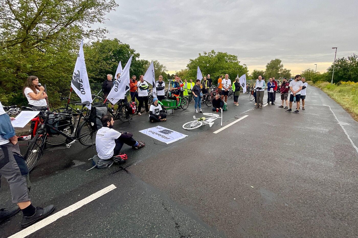 Menschen sitzen bei einer Mahnwache auf dem Boden weiße Vision Zero Fahnen