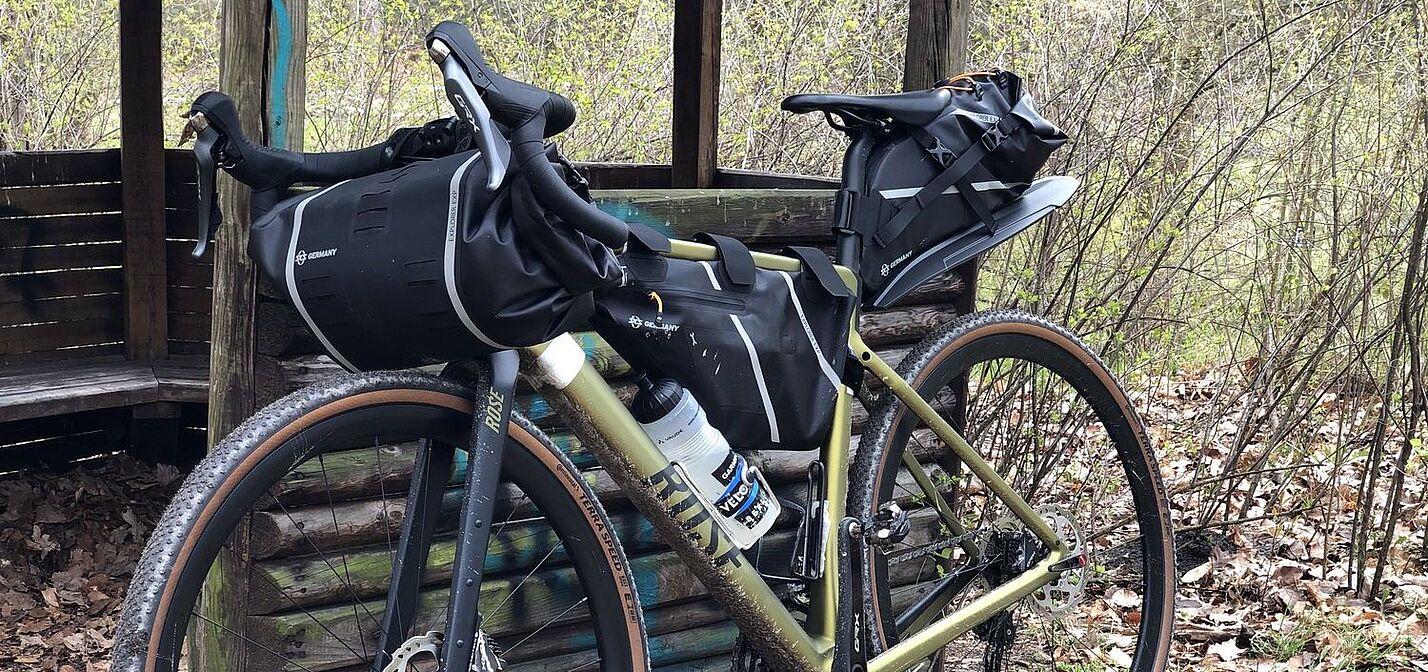 Ein Gravelbike mit Packtaschen lehnt an einer Schutzhütte im Wald. 