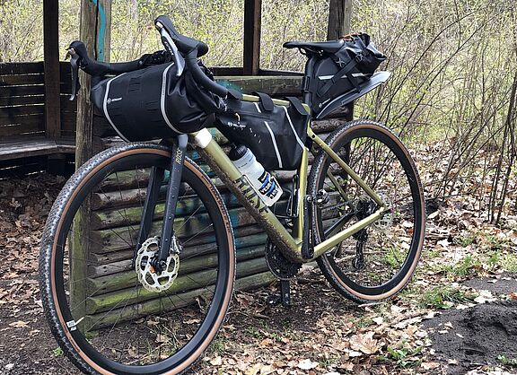 Ein Gravelbike mit Packtaschen lehnt an einer Schutzhütte im Wald. 