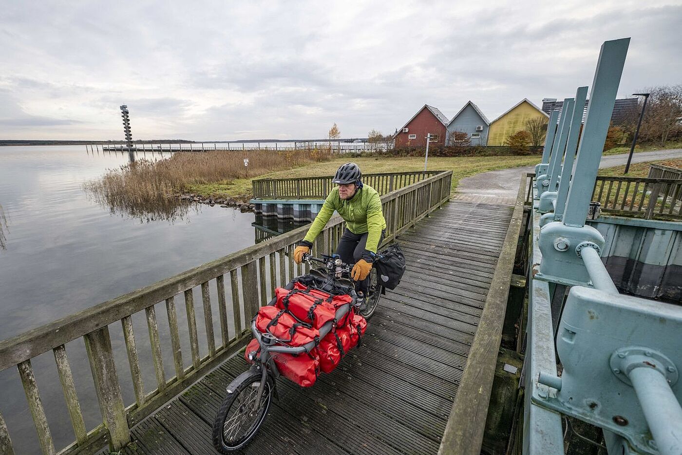 Gunnar Fehlau fährt auf seinem Lastenrad auf einem Bohlenweg am Wasser entlang. 