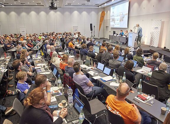 von Heesen Ein grpßer Saal mit 140 Menschen an Tischreihen, die zur Bühne blicken, wo Boris von Heesen einen Vortrag hält.