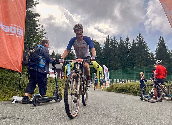 happy im ziel Ein mit schlamm bespritzter Mountainbiker hat gerade einen Zielbogen passiert und lächelt.