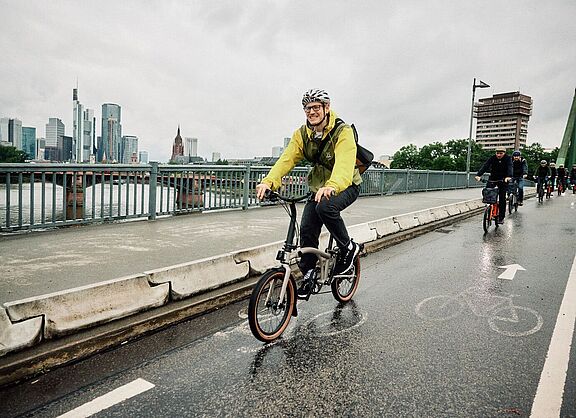 Radfahrer auf einem Brompton G-Line bei regenerischem Wetter in der Stadt. 