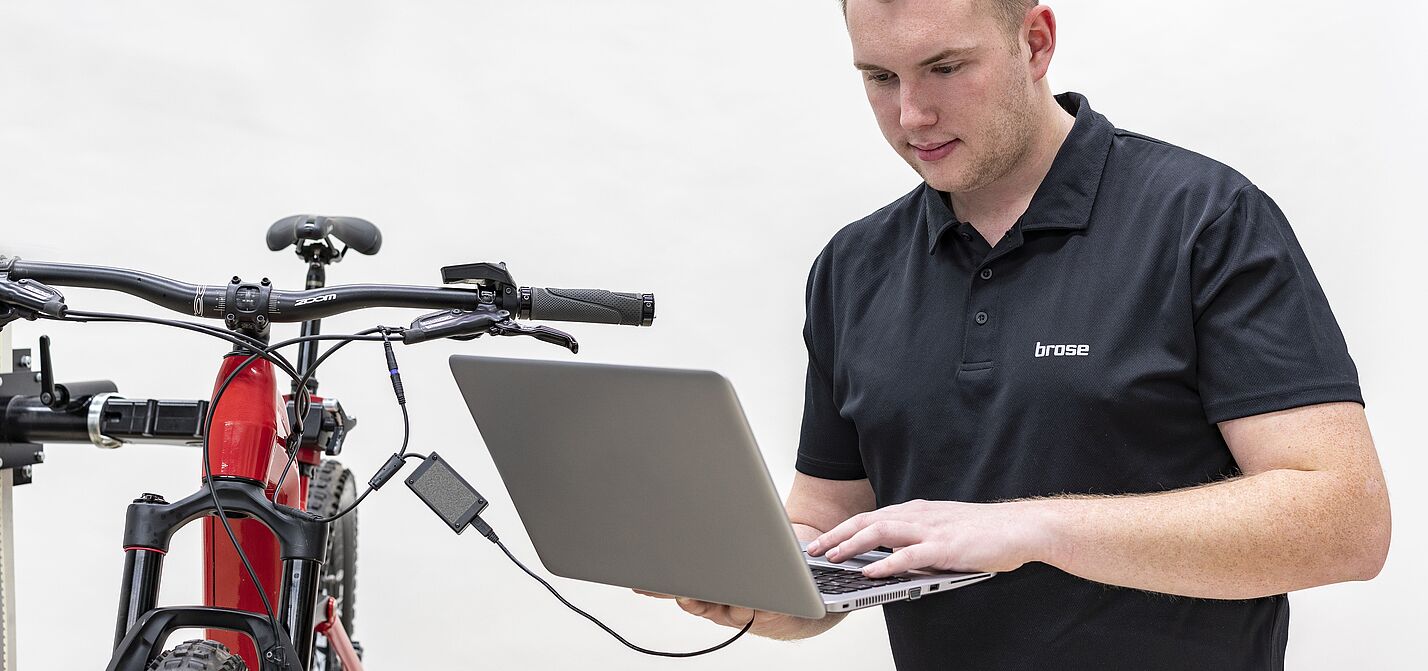 Mann mit Laptop steht neben einem Fahrrad. Das Laptop ist an das Fahrrad angeschlossen. Der Mann liest die elektronisch verfügbaren Daten mit seinem Laptop vom Fahrradmotor aus.