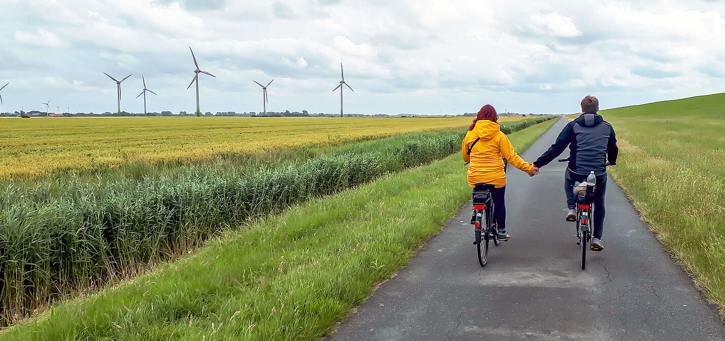 Zwei Radfahrende fahren auf einem asphaltierten Deichweg