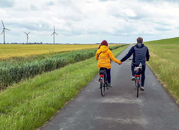 Zwei Radfahrende fahren auf einem asphaltierten Deichweg