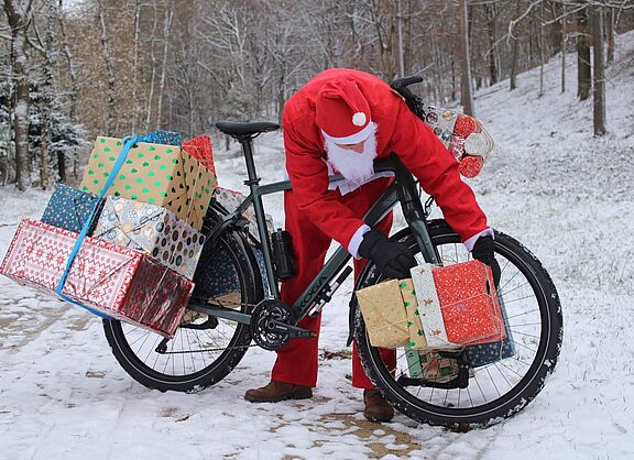 Weihnachtsmann Man in Weihnachtskleidung beugt sich über ein mit Geschenken beladenes Fahrrad im Schnee.