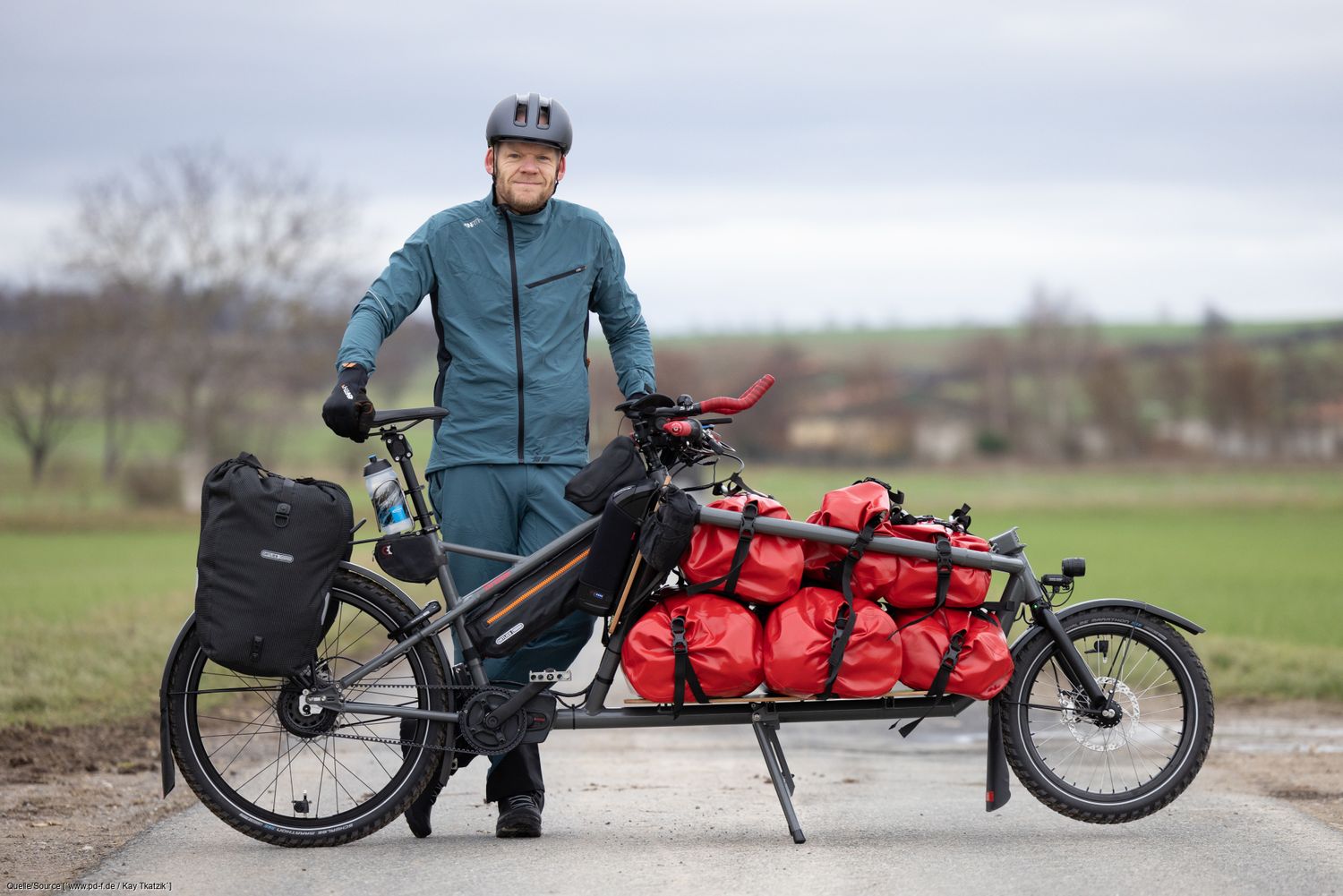 Gunnar Fehlau steht in Fahrradkleidung, vor ihm sein Lastenrad, mit dem er auf Workpacking-Tour ist. 